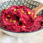 A bowl of roasted beetroot hummus garnished with some pine nuts.