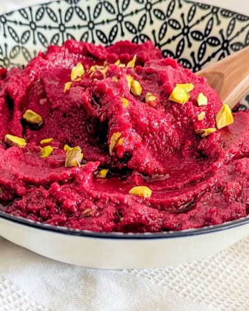 A bowl of roasted beetroot hummus garnished with some pine nuts.
