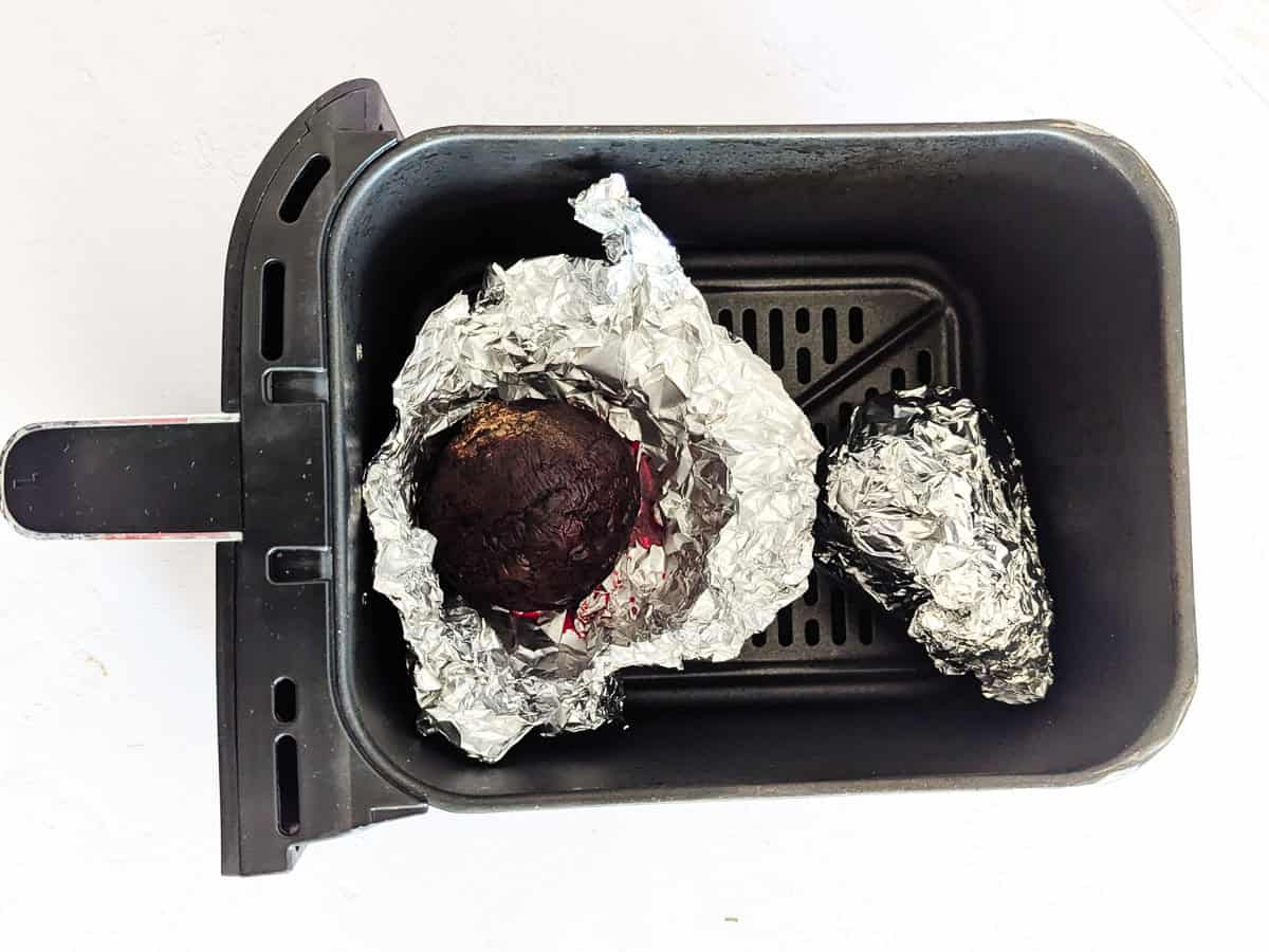 Beetroots wrapped in foil inside an air fryer basket.
