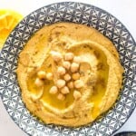 A bowl of hummus garnished with some olive oil and a handful of chickpeas.