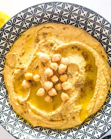 A bowl of hummus garnished with some olive oil and a handful of chickpeas.