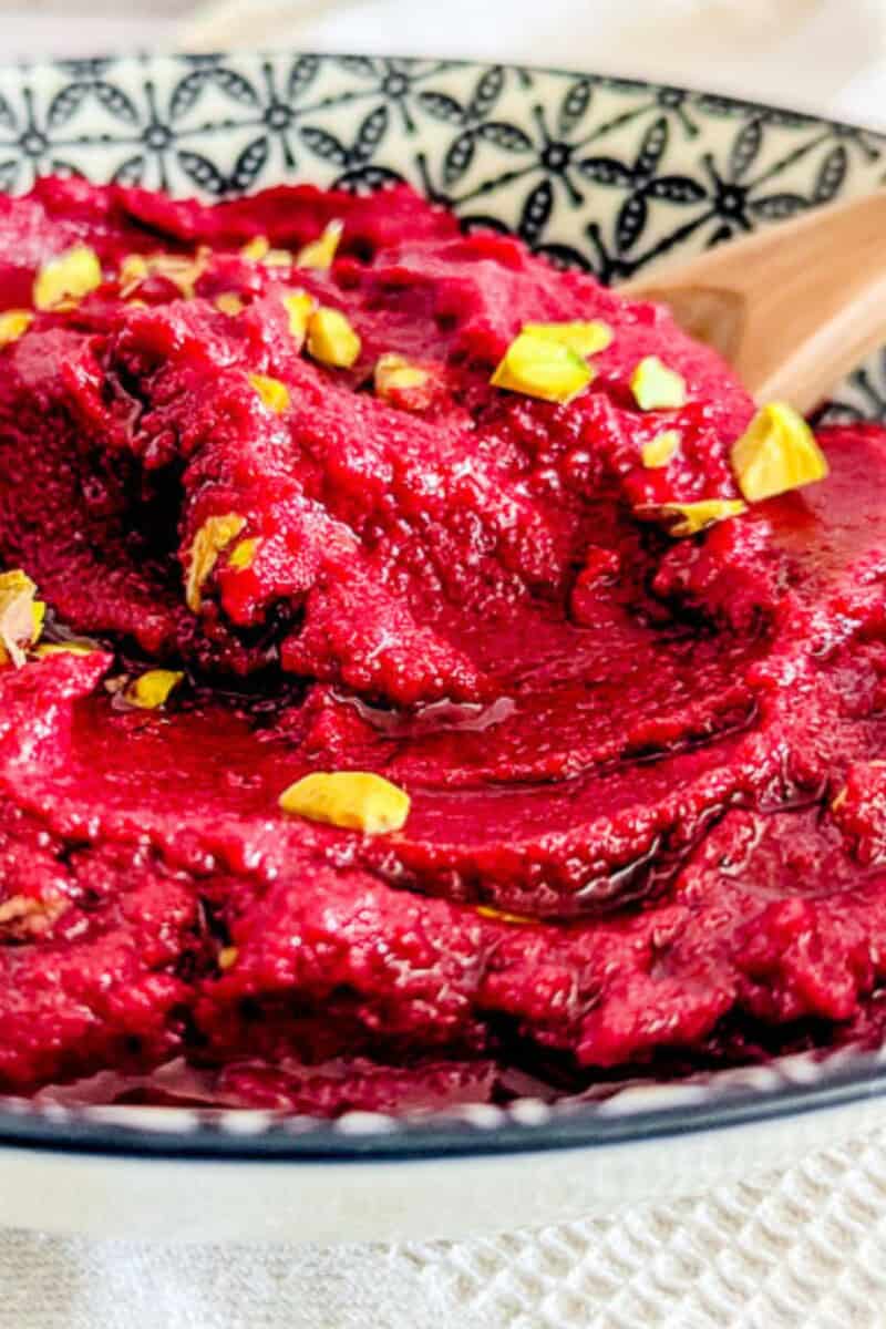 A bowl of beetroot hummus with a wooden spoon.