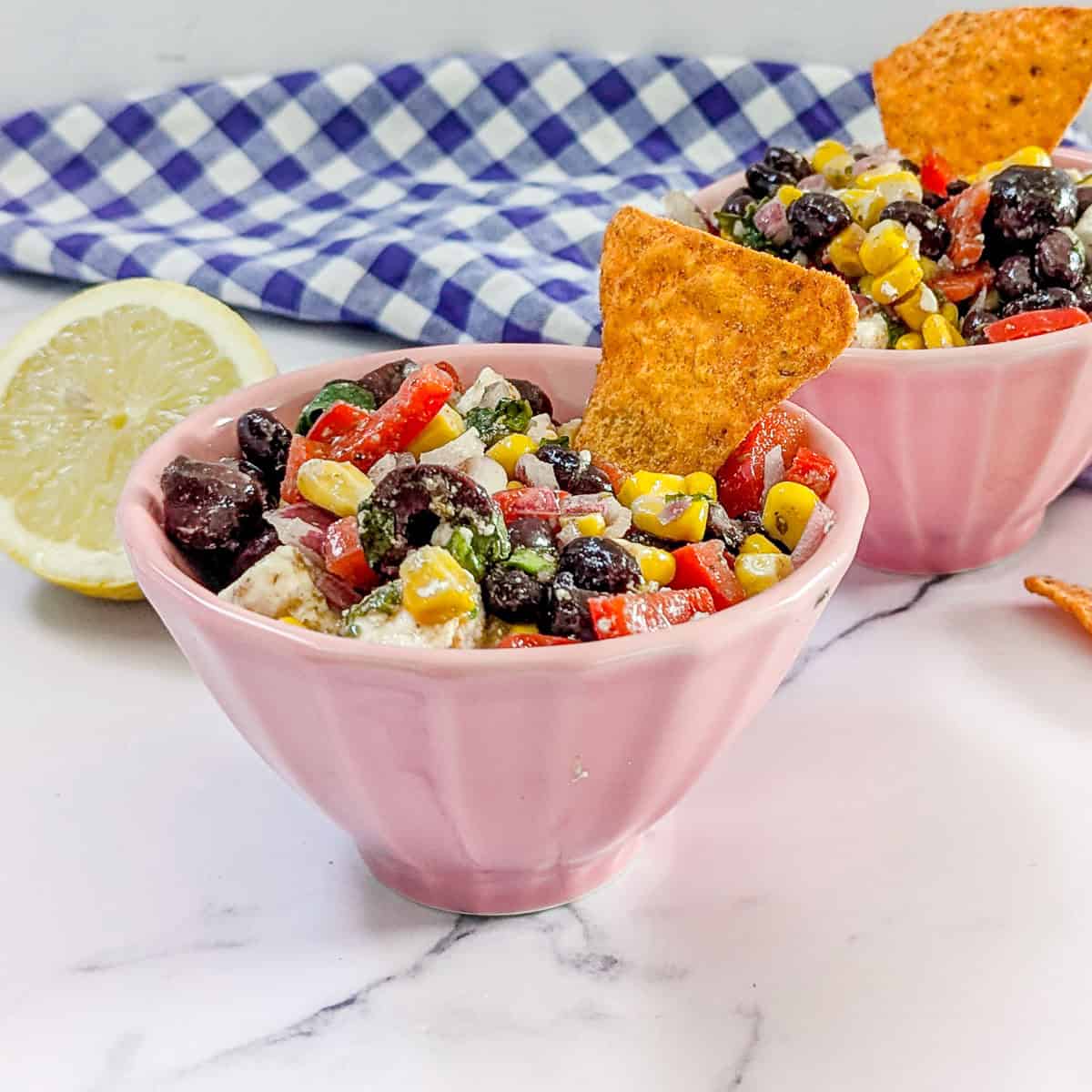 Two bowls of bean and corn dipp and a lemon wedge.