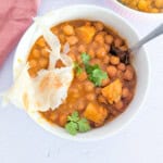 Two bowls of chickpea and potato stew with some roti on top.