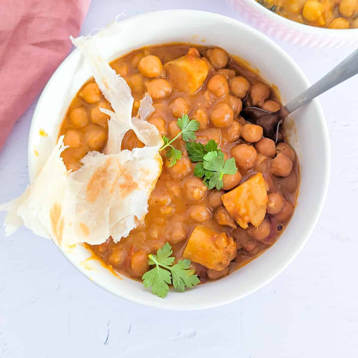Two bowls of chickpea and potato stew with some roti on top.