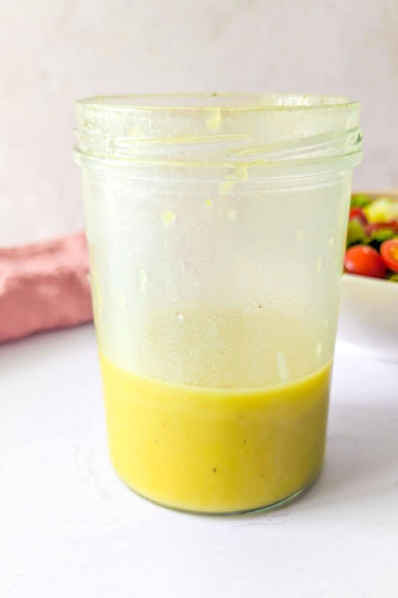 A jar of lemon and olive oil dressing next to a bowl of salad.