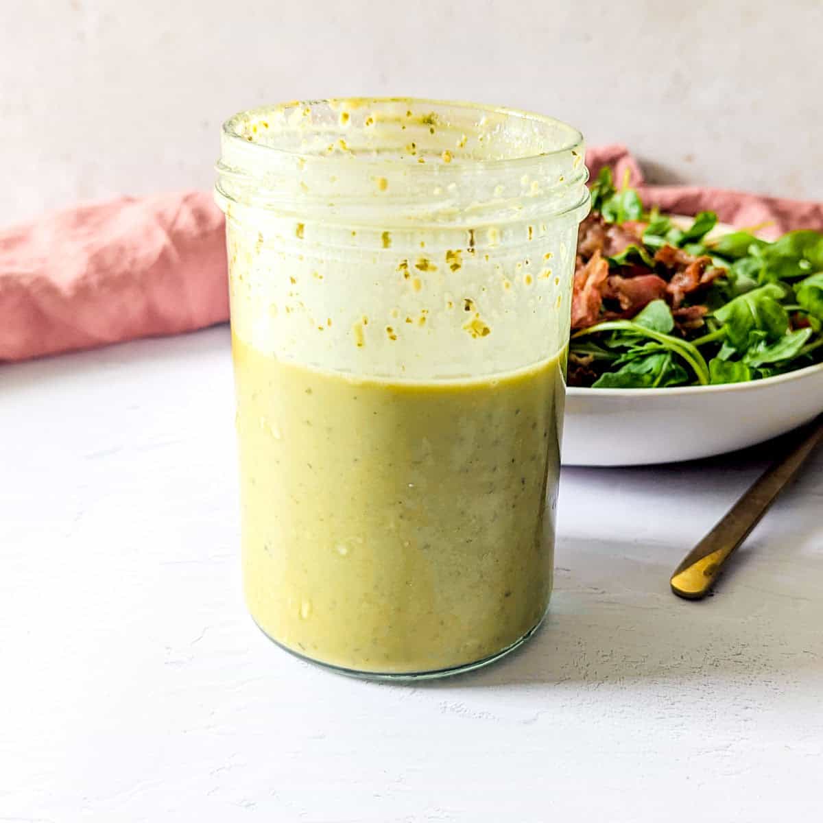 Pesto balsamic salad dressing in front of salad greens with bacon.