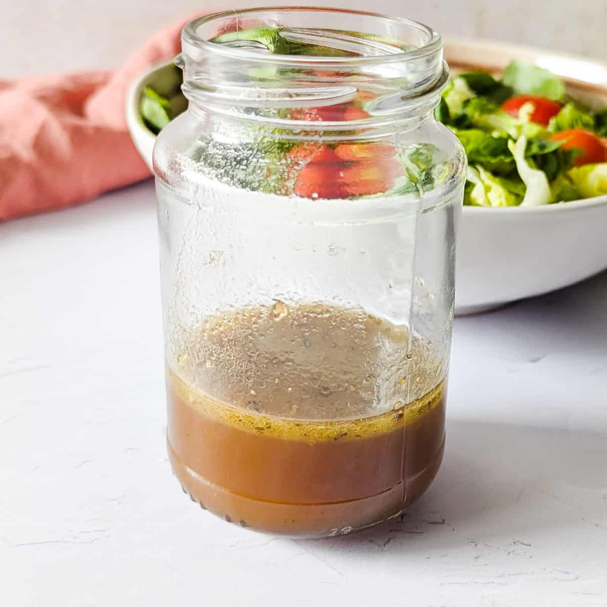 A jar of balsamic dressing next to a salad bowl.