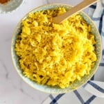 Close-up of yellow Mediterranean rice in a patterned bowl with a wooden spoon, showing texture and spices.