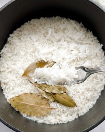 Stovetop basmati rice in a black pot with bay leaves.