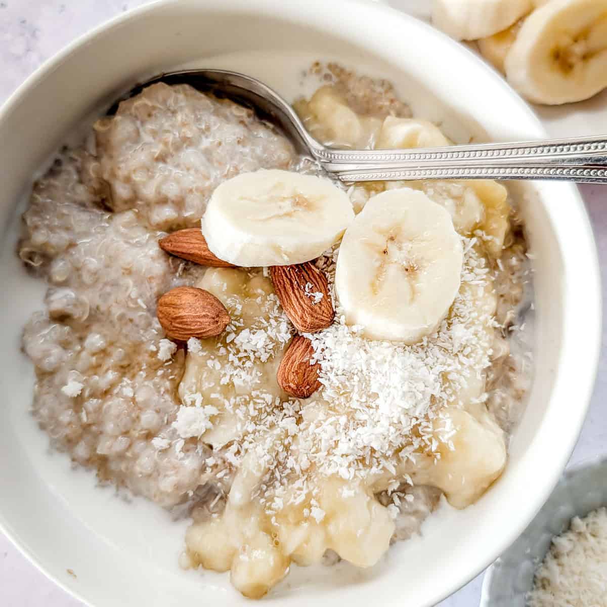 Quinoa amaranth porridge in a bowl, garnished with banana slices and some almonds.