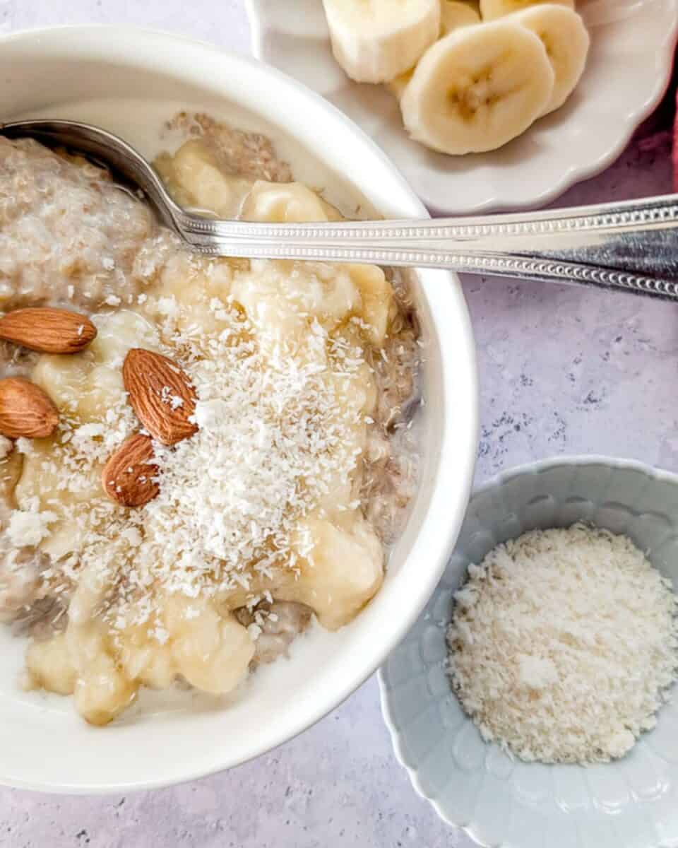Zoomed-in bowl of creamy quinoa and amaranth porridge topped with banana, coconut, and almonds.