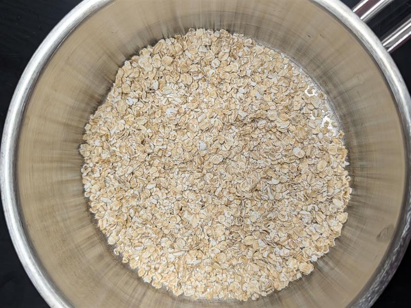 Uncooked rolled oats in the bottom of a stainless steel pot.
