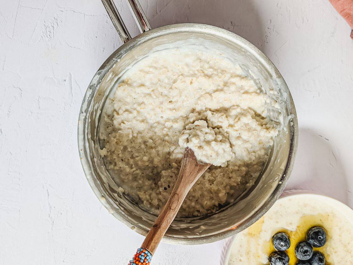 Oats porridge inside a pot with a wooden serving spoon.