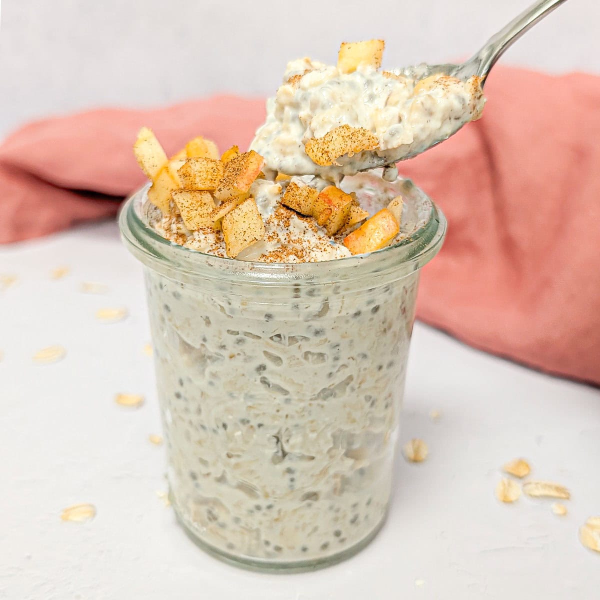 Apple cinnamon overnight oats in a glass jar topped with diced apples and cinnamon, with a spoonful lifted.