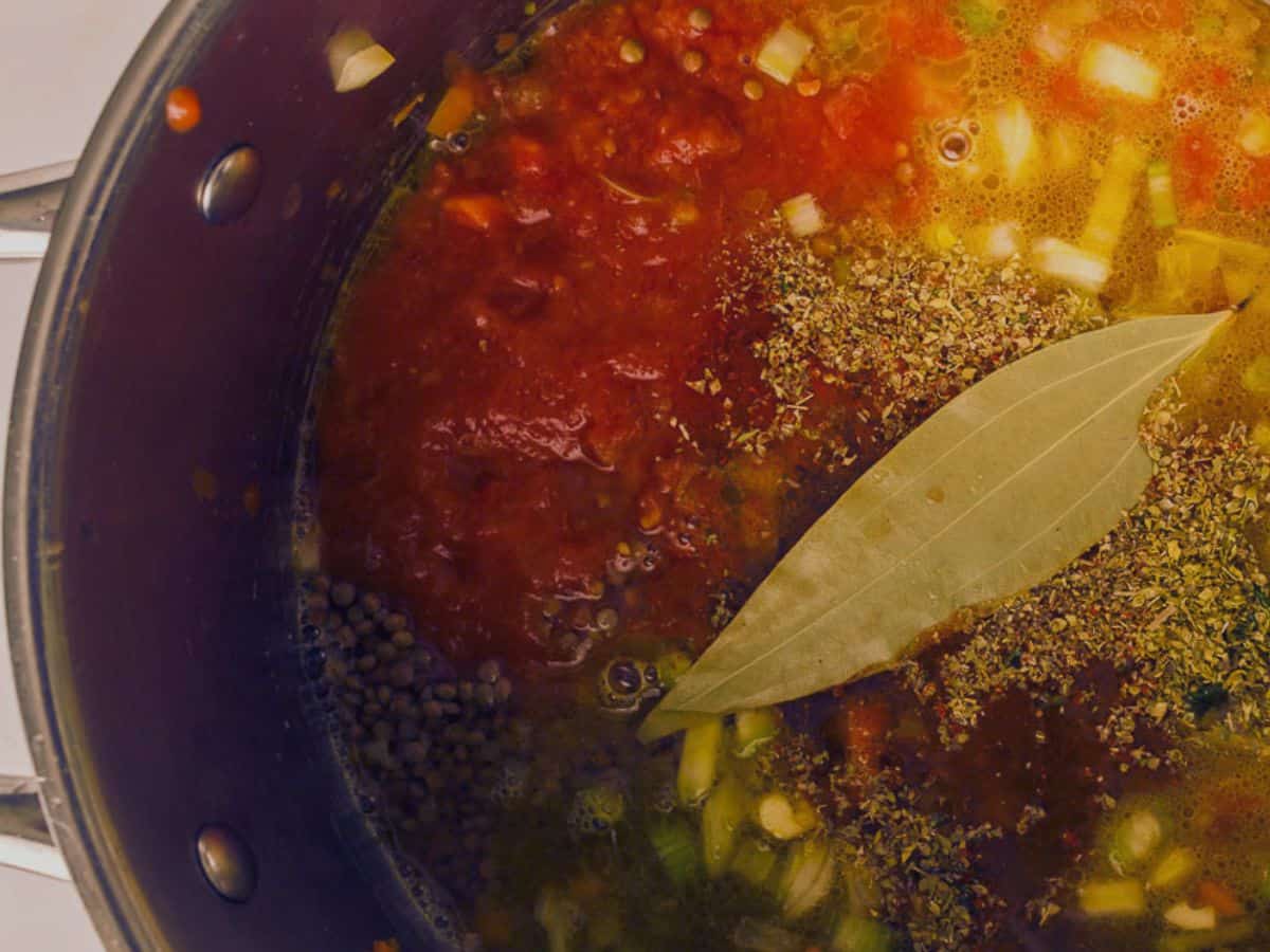 Lentils cooking in a pot along with tomatoes, broth, seasonings, and some bay leaves.