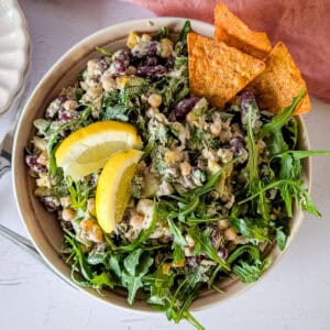 Chickpea and tuna salad with avocado and arugula with some tortilla chips and lemon wedges.