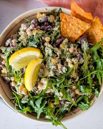 Chickpea and tuna salad with avocado and arugula with some tortilla chips and lemon wedges.