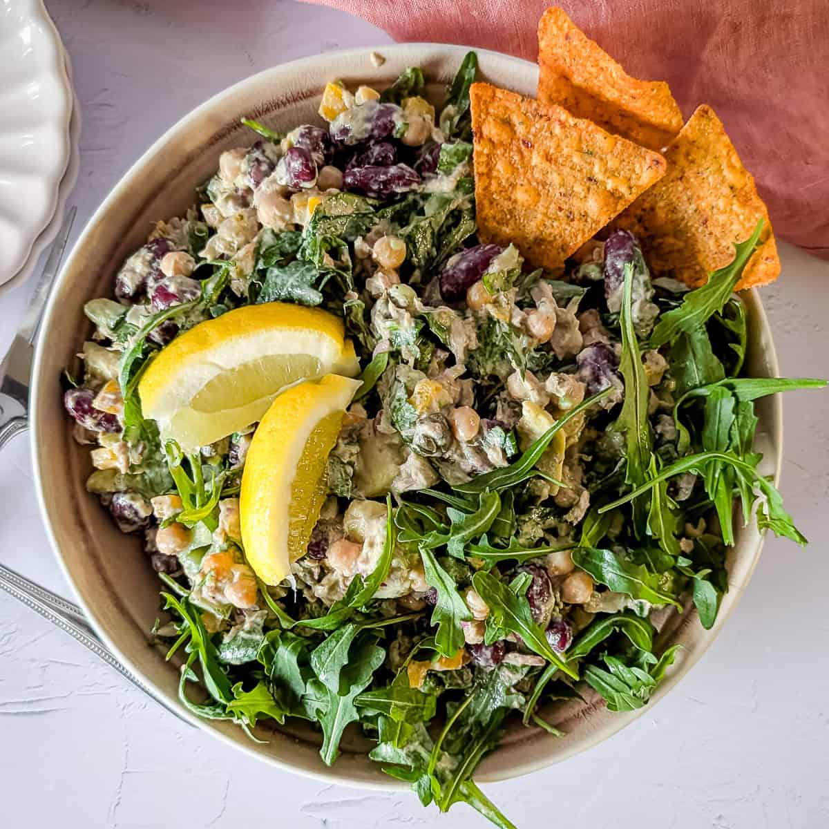 Chickpea and tuna salad with avocado and arugula with some tortilla chips and lemon wedges.