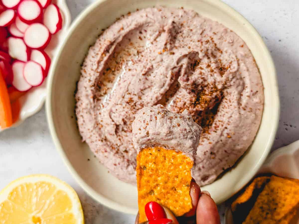 Top-down image of red kidney bean hummus served in a cream-colored bowl.