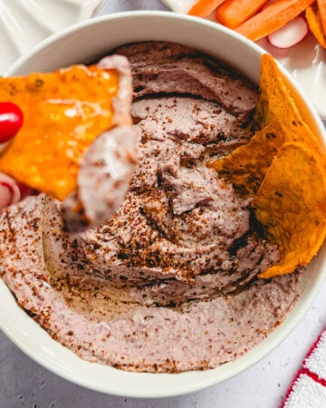 Creamy red kidney bean hummus served in a bowl with tortilla chips and fresh vegetables.