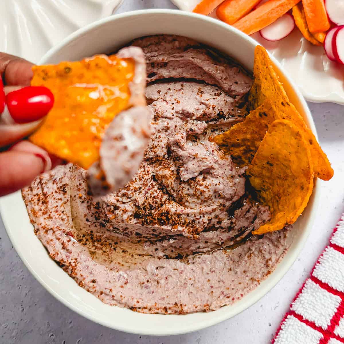 Creamy red kidney bean hummus served in a bowl with tortilla chips and fresh vegetables.