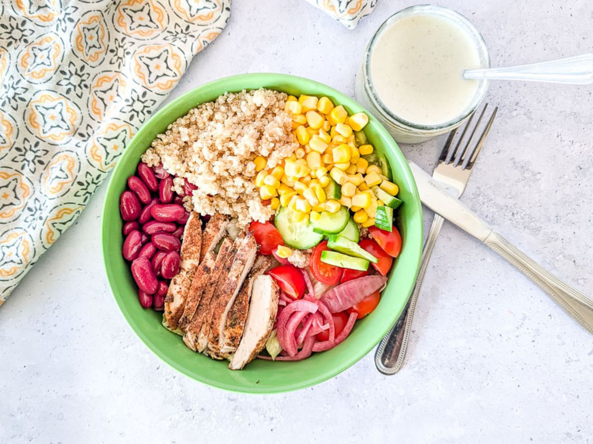Mediterranean grilled chicken bowl with cucumber, tomatoes, olives, and feta, assembled and ready for dressing.