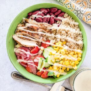 Mediterranean chicken grain bowl with quinoa, kidney beans, sweet corn, cucumber, tomatoes, and yogurt dressing.