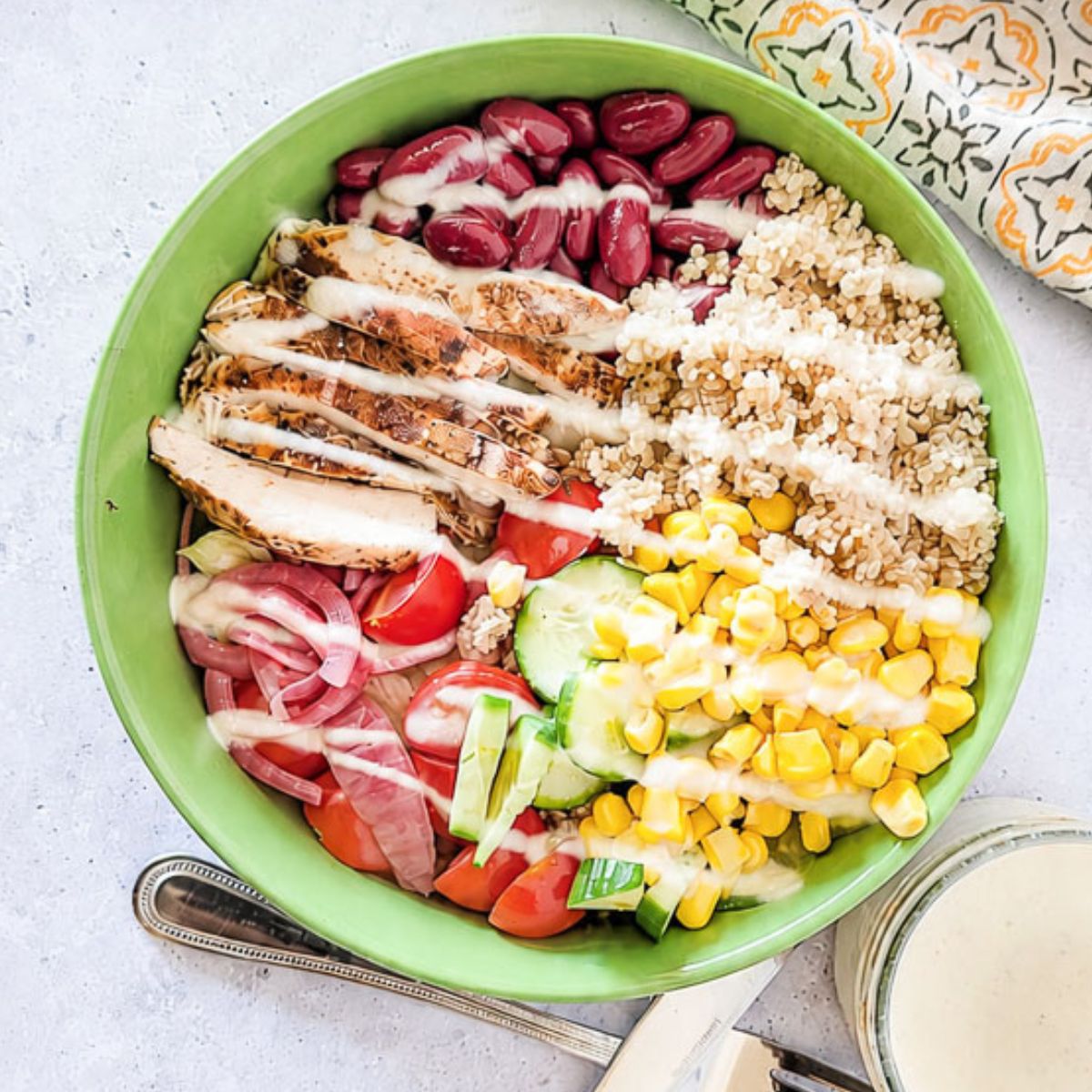 Mediterranean chicken grain bowl with quinoa, kidney beans, sweet corn, cucumber, tomatoes, and yogurt dressing.