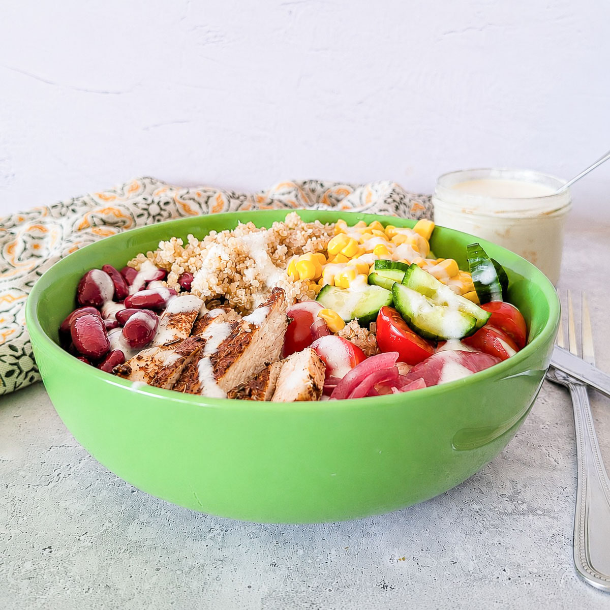 Side view of a Mediterranean chicken grain bowl with quinoa, vegetables, and yogurt dressing.