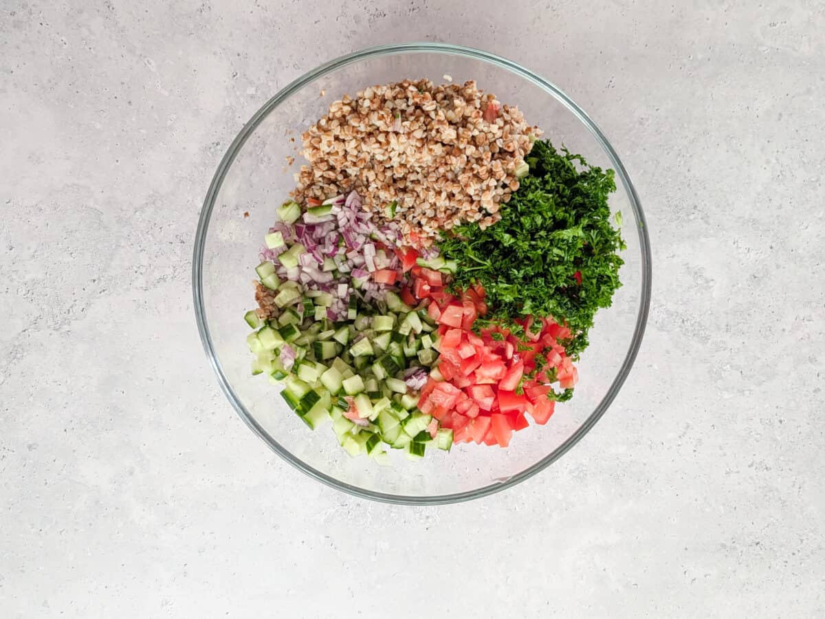 A top-down image of buckwheat with chopped vegetables and parsley in a glass bowl.