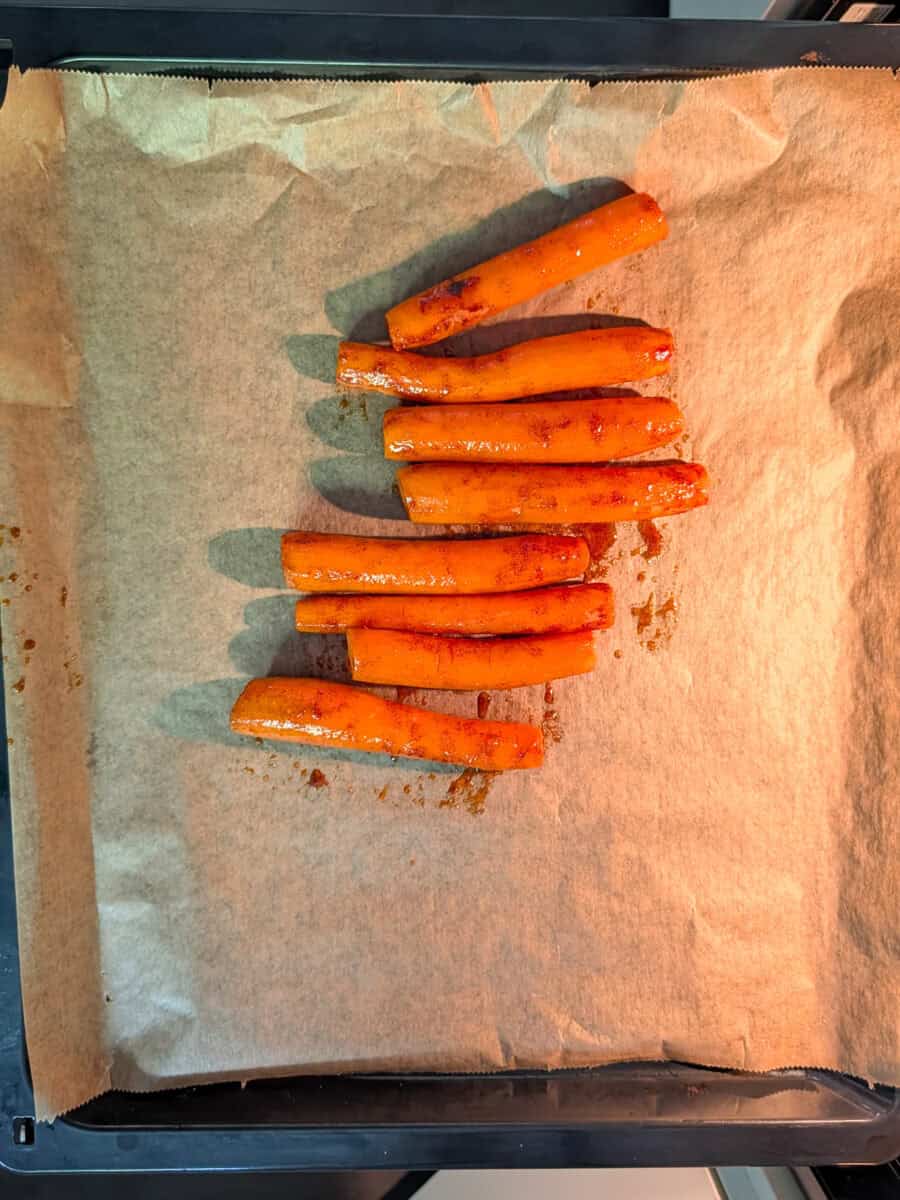 A top-down image of seasoned carrots arranged on a baking tray.
