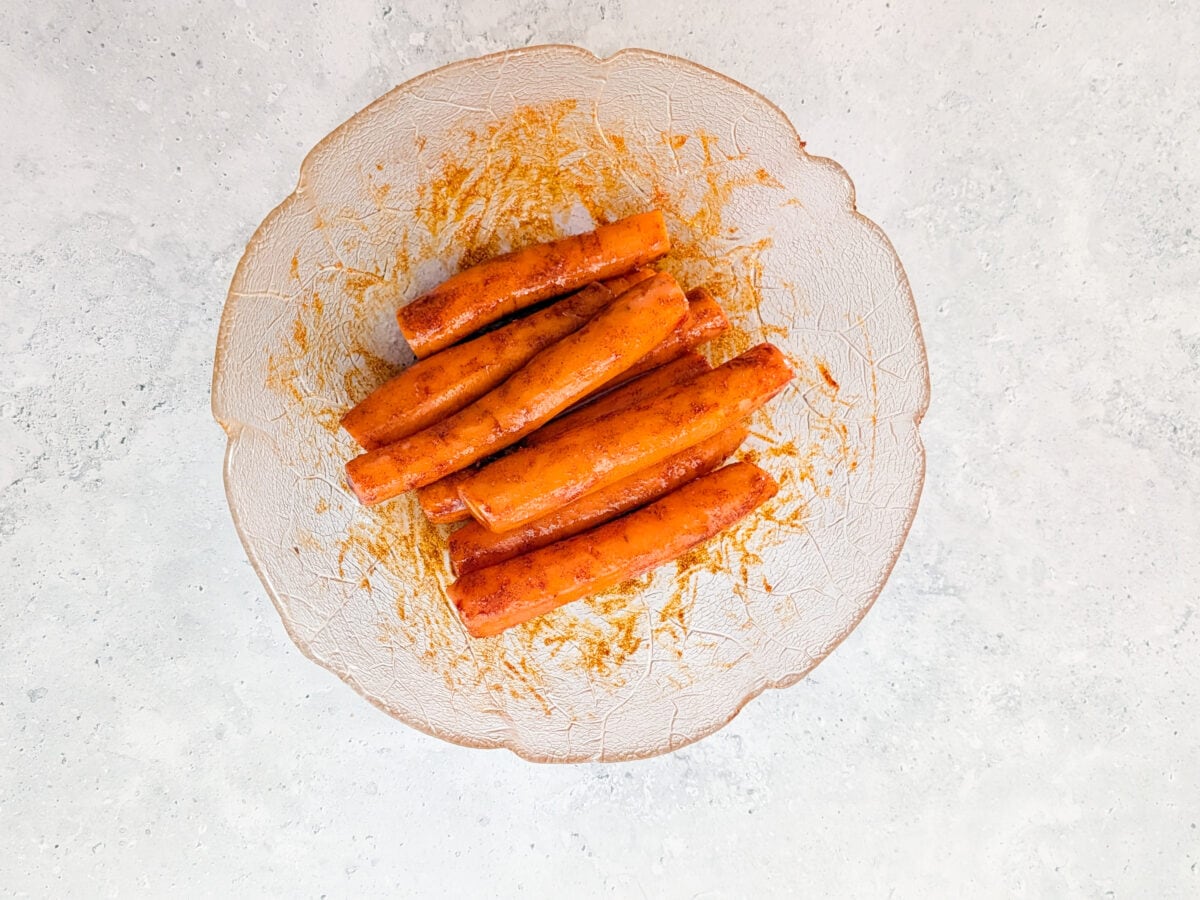 A close-up image of peeled and seasoned carrots inside a glass bowl.