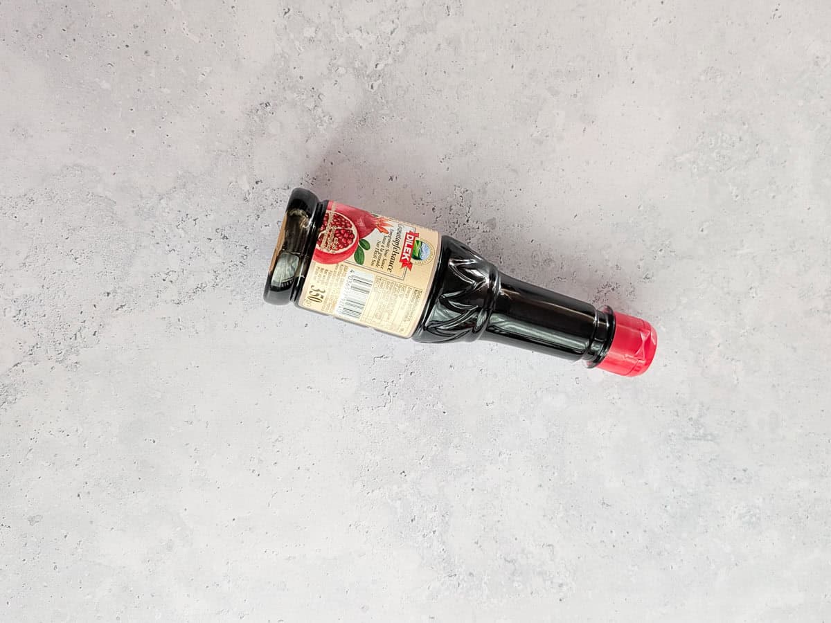 A bottle of pomegranate molasses lying flat on a grey countertop.