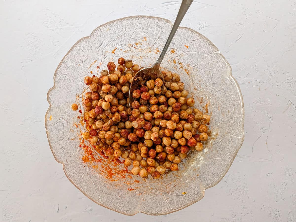 A close-up image of cooked chickpeas seasoned with spices in a glass bowl.