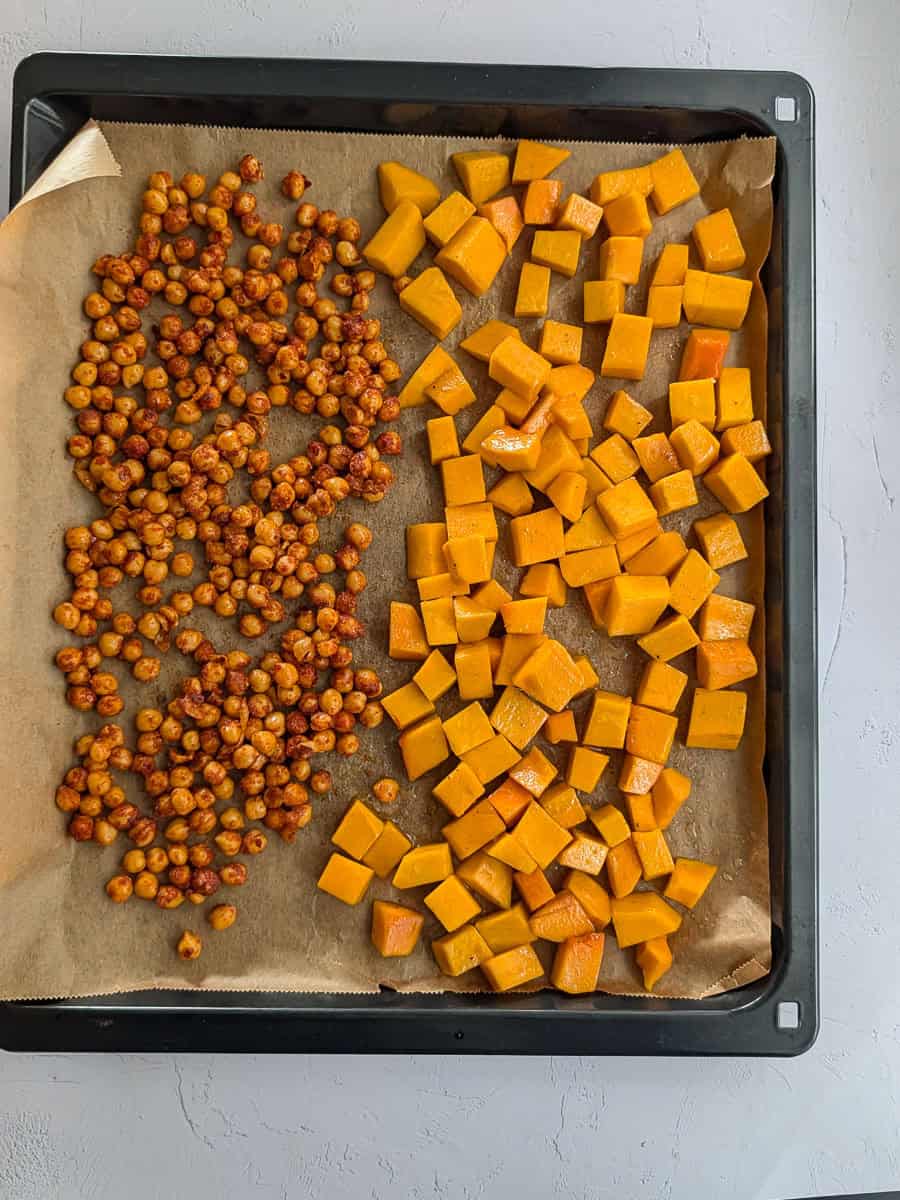 An overhead image of seasoned chickpeas and cubed pumpkin on a baking tray ready for roasting.